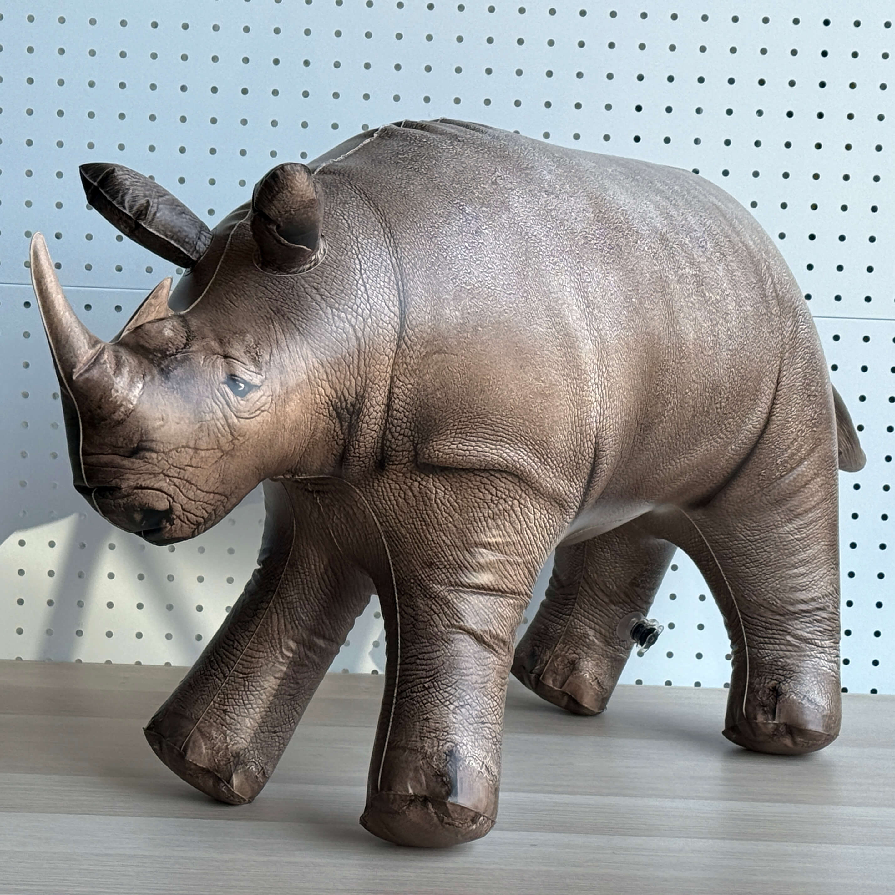 Jet Creations inflatable Realistic rhinoceros model on a wooden surface with a pegboard background