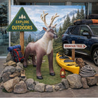 Reindeer statue with outdoor gear, car, and signs in front of a mountainous landscape.